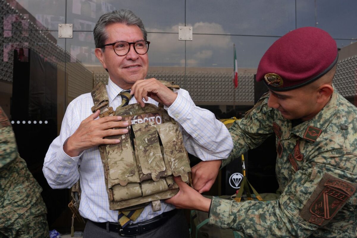 Ricardo Monreal ajusta un chaleco táctico con ayuda de un militar durante una exhibición.